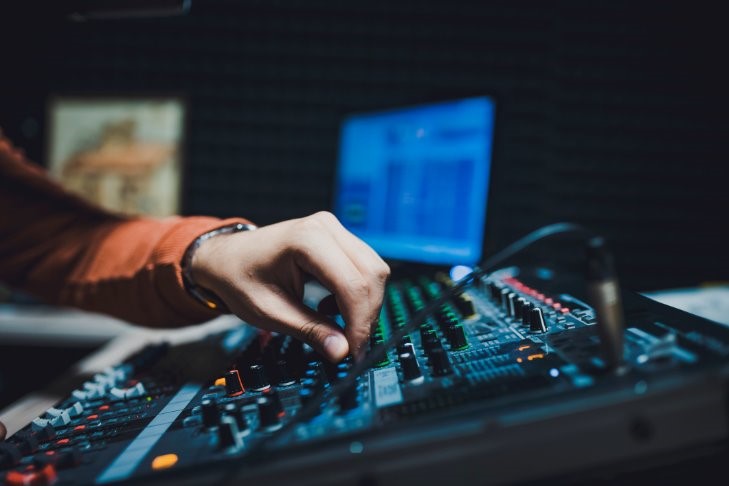 A hand adjusting a dial on an audio mixing board